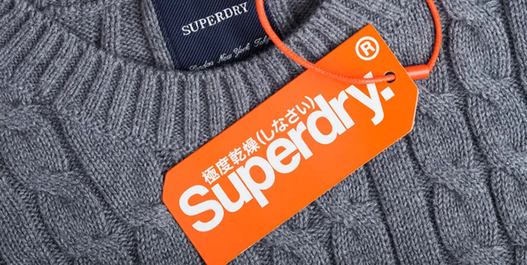 Close-up of a grey knit sweater with a Superdry label and an orange Superdry tag featuring white text in English and Japanese.