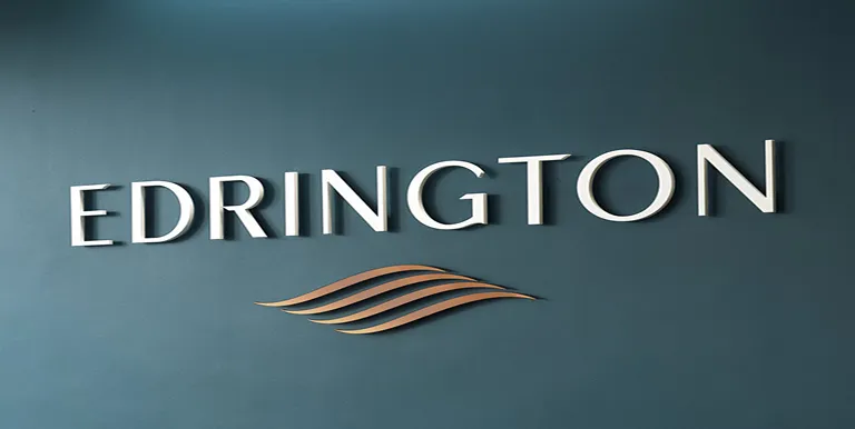 The image shows the word EDRINGTON in large, white, capital letters on a blue wall, with a stylized gold wave design beneath the text.